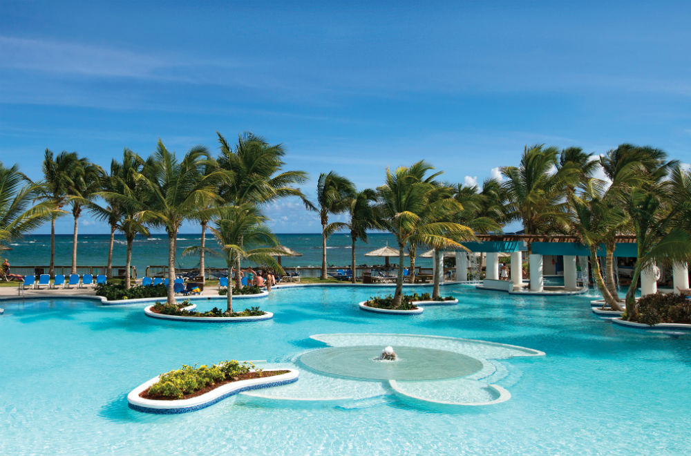 Resort pool with palm trees and ocean in background